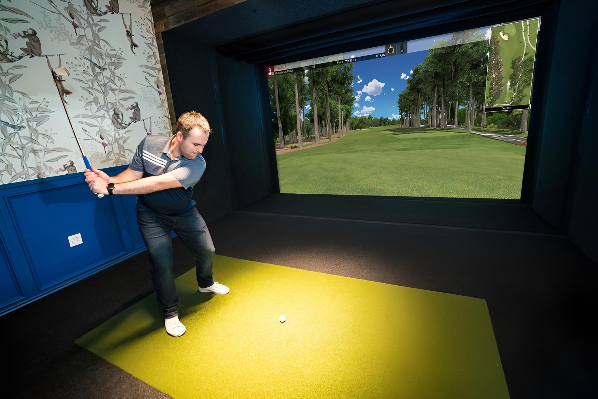 Indoor golf simulator setup with a large screen, golf clubs, and a putting green area.